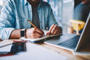 homem sentado à mesa de escritório anotando em um caderno