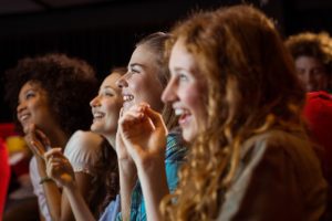 quatro moças olhando para a tela do cinema sorrindo com ingressos pagos pelo Ticket Cultura