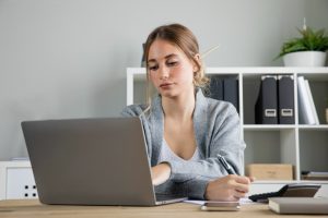 Mulher sentada à mesa de trabalho olha de maneira desinteressada para seu laptop, evidenciando quit quitting