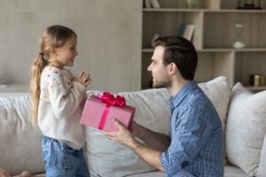 Menina sendo recebendo uma caixa de presente cor-de-rosa de um adulto