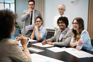 Uma funcionária falando enquanto seus colegas de trabalho escutam em uma sala de reunião