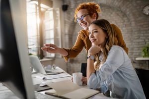 Duas mulheres no ambiente corporativo trabalhando em harmonia e sorrindo juntas
