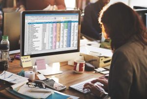 Mulher fazendo cálculos em planilha do excel em frente ao computador