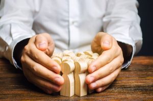 Mãos de um executivo protegendo bonecos de madeira que representam os talentos de sua companhia