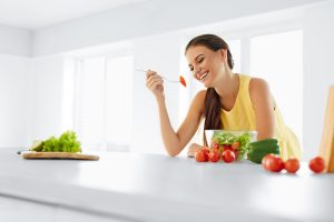 mulher sorri encostada ao balcão enquanto come salada