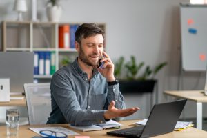Homem sentado em frente ao computador fala ao telefone