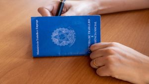 Mãos femininas assinam uma carteira de trabalho pós demissão.