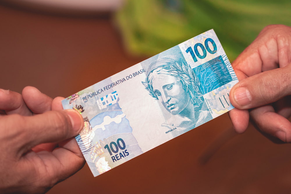 homem paga outra pessoa com uma nota de cem reais