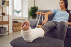 mulher com perna quebrada engessada sentada no sofá