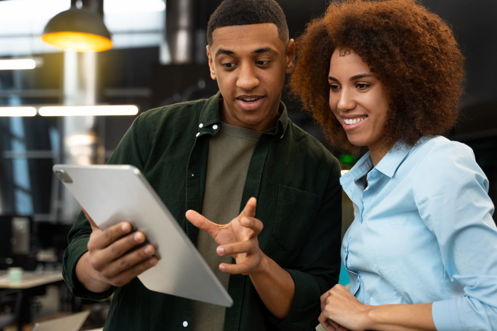 dupla de gestores negros composta por um homem e uma mulher conversando enquanto olham um tablet