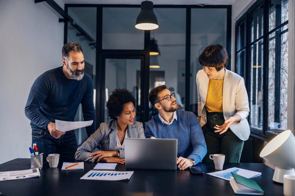 grupo de quatro colaboradores diversos olham atentamente para um notebook