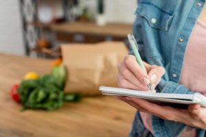 Mulher faz lista de compras em casa para economizar vale-alimentação