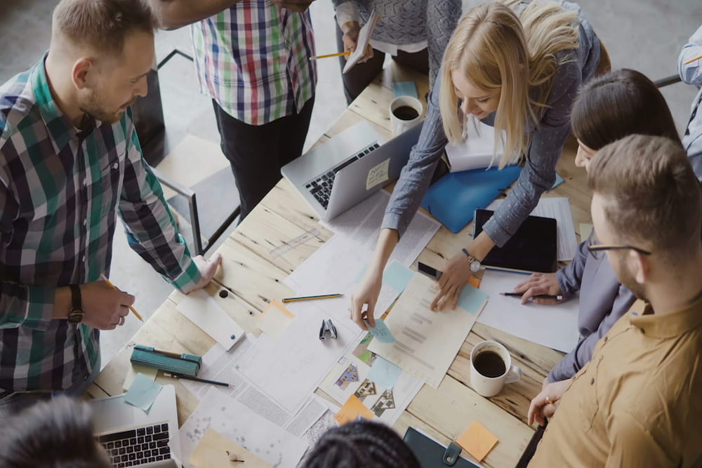 Vista superior do grupo de pessoas em pé perto da mesa. Equipe de negócios jovem trabalhando juntos em projeto