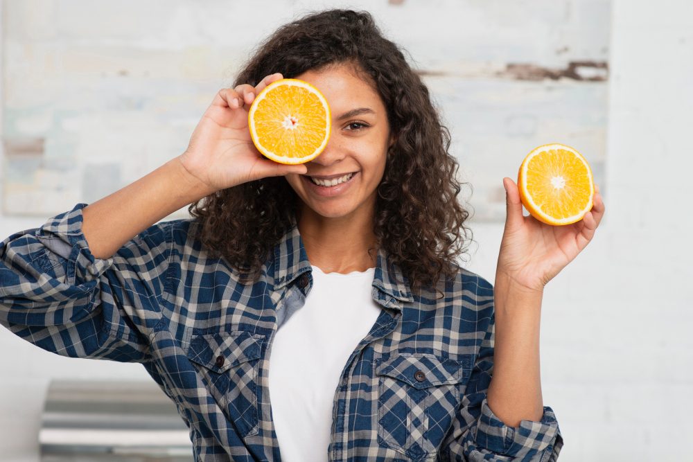 Mulher segurando duas laranjas cortadas ao meio