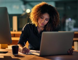 mulher sentada à mesa em frente ao seu laptop fazendo apontamentos sobre recursos financeiros 