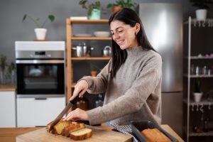 Mulher jovem corta pão na bancada de sua cozinha