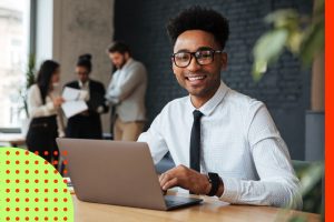 Contador olha sorridente para a câmera sentado em frente ao seu laptop e comemora o dia do contador