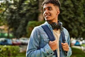 Jovem em pé com mochila e fones de ouvido andando na rua