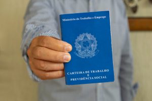 Homem em pé segura sua carteira de trabalho fechada, simbolizando a legislação acerca do aviso de férias