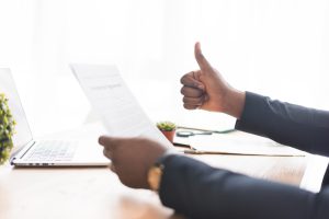 Homem sentado segurando um papel com uma mão e fazendo gesto de positivo com outra
