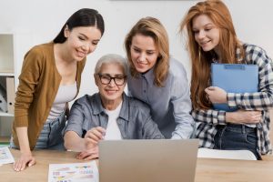 três jovens estão em pé atrás e ao lado de uma mulher idosa no computador