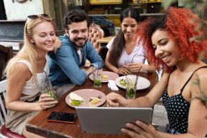 Quatro jovens sentados à mesa fazem uma refeição e olham para o tablet pesquisando se quando sai de férias recebe Ticket