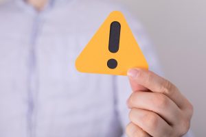Mão de uma pessoa segurando um triângulo amarelo com ponto de exclamação dentro, sinalizando atenção