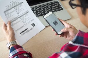 Homem com celular numa mão e conta na outra mostra como pagar conta com o Ticket Super Flex