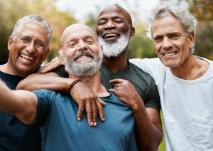 Quatro homens acima dos 60 anos abraçados sorriem 