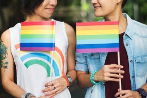 Duas pessoas olham-se enquanto seguram bandeiras do arco-íris, simbolizando o orgulho LGBTQIAP+