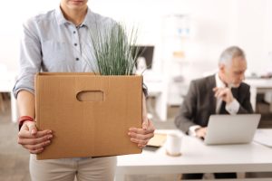 Homem em primeiro plano carregando caixa de papelão após demissão por insubordinação no trabalho