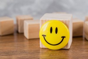 Sobre uma mesa, vemos três cubos de madeira. Em primeiro plano, um dos cubos tem um emoji de sorriso amarelo