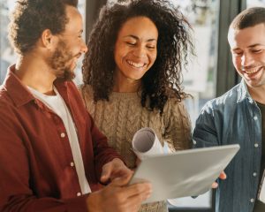 Dois homens e uma mulher em pé leem algo num papel e sorriem