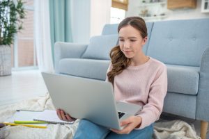 mulher sentada no tapete da sala de sua casa praticando blended learning ao estudar via computador 