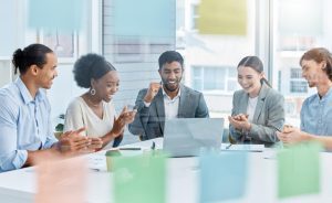 Três pessoas animadas em mesa de reunião demonstram diferentes competências