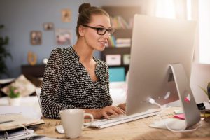 Mulher sentada olha animadamente para computador enquanto digita