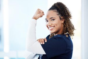 Mulher sorrindo faz pose de imagem icônica feminista, com braço esquerdo flexionado enquanto o direito o apoia