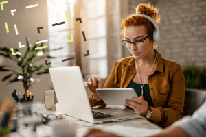 Mulher sentada à mesa do escritório com fones de ouvido e tablet praticando blended learning