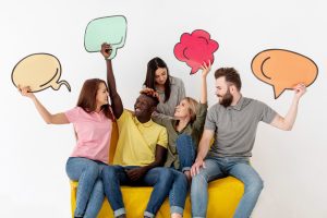 Cinco pessoas sentadas em sofá amarelo carregam placas de diálogo