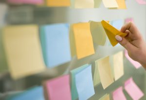 Diversos post-its em painel espelhado e alguém descolando um deles