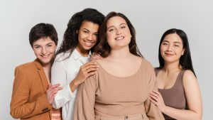 Quatro mulheres abraçam-se olhando para a câmera de maneira confiante, simbolizando a proteção das mulheres no mercado de trabalho