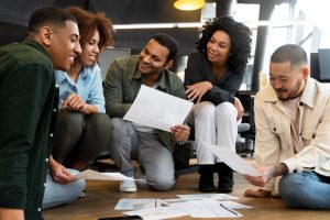 Equipe multifuncional de cinco pessoas sentadas no chão analisam papeis
