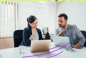 Mulher e homem sentados ao mesa em frente aos respectivos computadores fazem job crafting