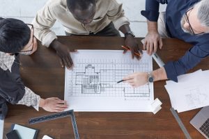 4 pessoas observam uma planta arquitetônica sobre a mesa