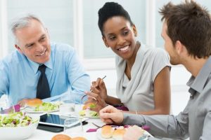 Uma mulher e dois homens almoçam sentados à mesa 