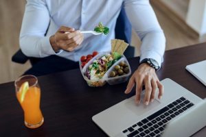 Homem come salada senado enquanto trabalha no seu notebook