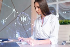 Mulher sentada à mesa do trabalho faz anotações e sobre ela há elementos visuais tecnológicos