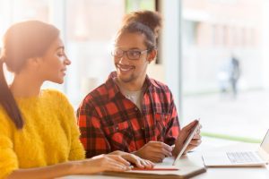 Dois jovens conversam animadamente sentados à mesa de trabalho