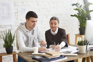 Homem e mulher sentados à mesa analisam documentos