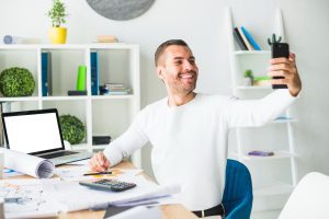 Homem faz selfie sentado à mesa de trabalho